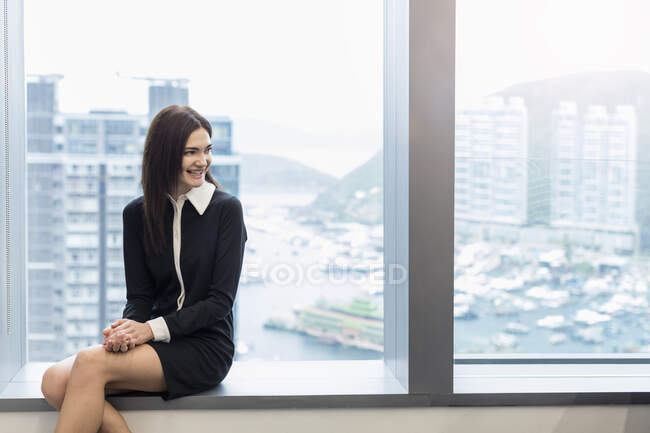 Frau sitzt auf Fensterbank und schaut lächelnd weg — Stockfoto