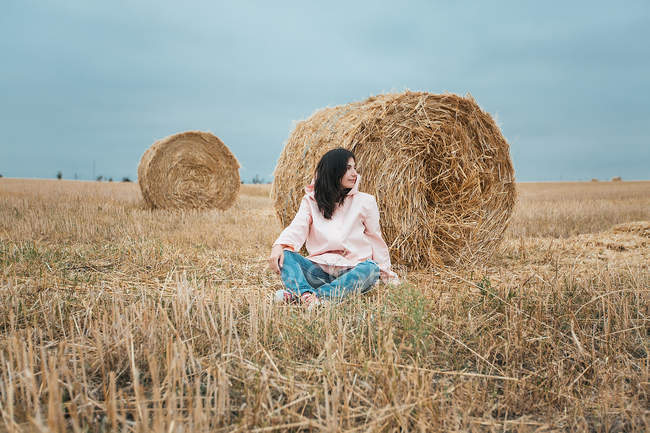 Женщина в розовом плаще сидит у стога сена — стоковое фото