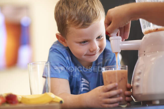 Mother pouring fruit smoothie for son in kitchen — Stock Photo