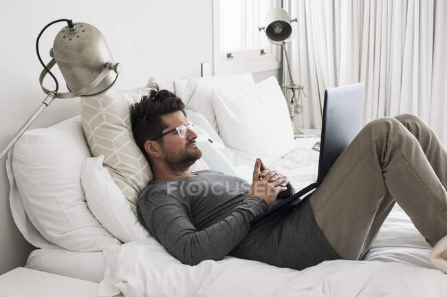 Homem adulto médio deitado na cama, usando laptop — Fotografia de Stock