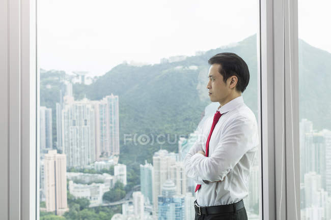 Empresario, brazos cruzados mirando por la ventana - foto de stock