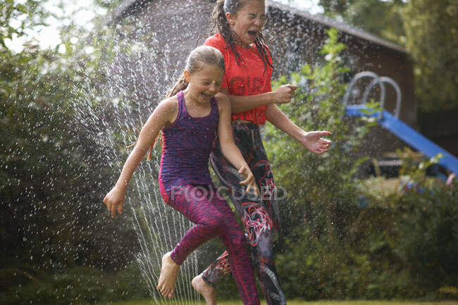 Girls jumping over garden sprinkler — Stock Photo