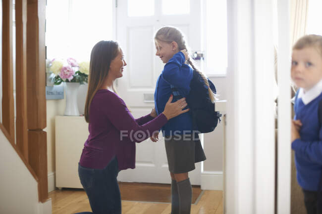 Mulher checando uniforme da escola da filha no corredor — Fotografia de Stock