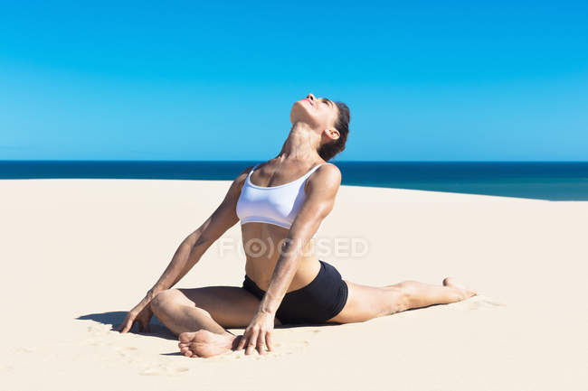 Woman on beach stretching in yoga position — Stock Photo