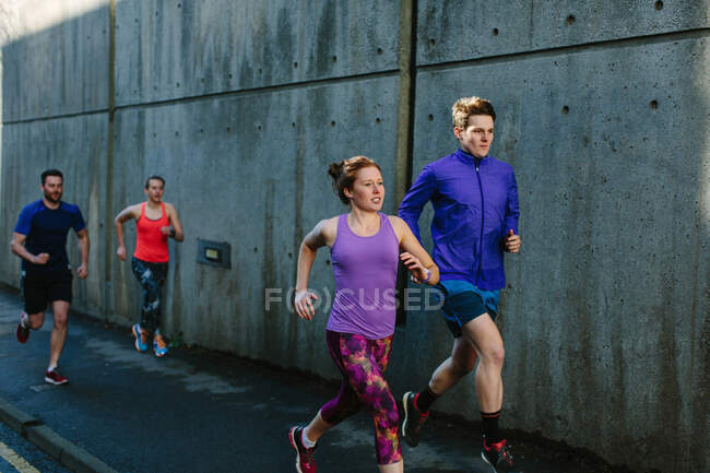 Quatro jovens corredores adultos correndo ao longo da calçada da cidade — Fotografia de Stock