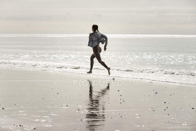 Молода жінка біжить босоніж по краю води на пляжі — стокове фото
