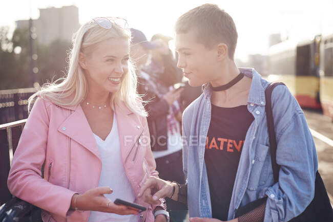 Two young female friends at sunlit city tram station — Stock Photo