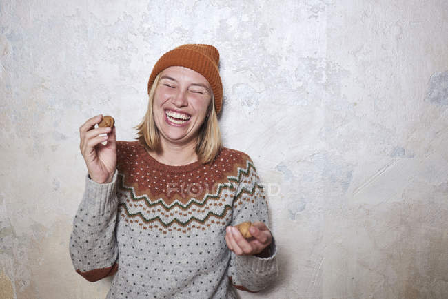Porträt einer Frau mit Pullover und Strickmütze, Walnüssen in der Hand, lachend — Stockfoto