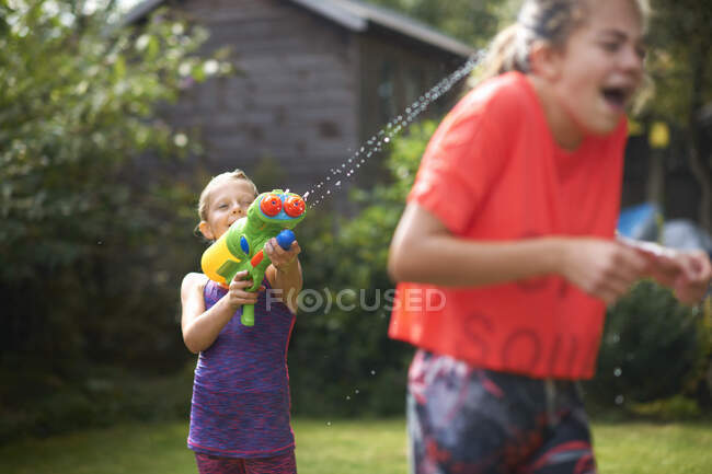 Мальчик брызгает своими сестрами-подростками водяным пистолетом в саду — стоковое фото
