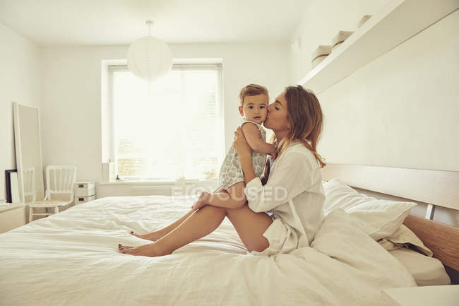 Mutter sitzt auf Bett und umarmt Kleinkind — Stockfoto