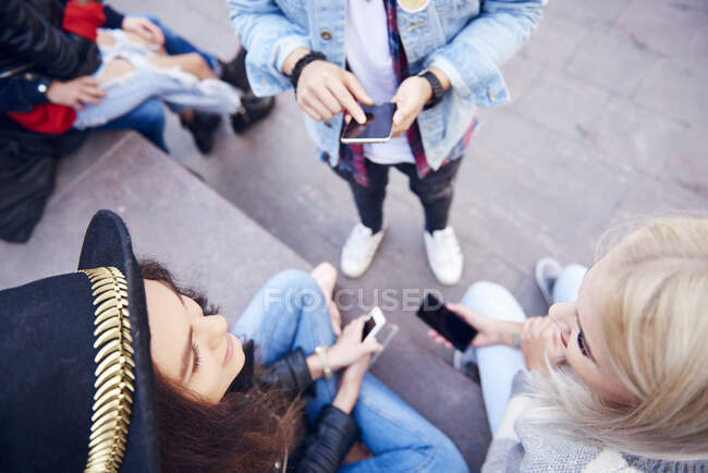 Overhead view of young adult friends looking at smartphone and talking on city stairs — Stock Photo
