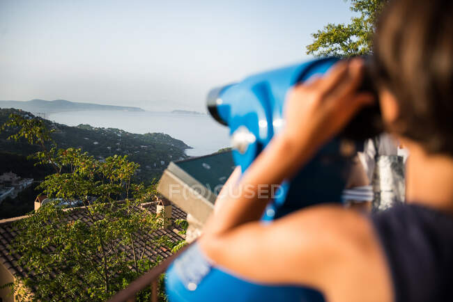 Over shoulder view of boy looking through coin operated binoculars at misty coastline landscape, Begur, Catalonia, Spain, — Stock Photo