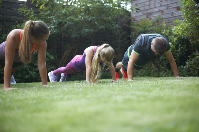 Familia haciendo flexiones y haciendo ejercicio en el jardín - foto de stock
