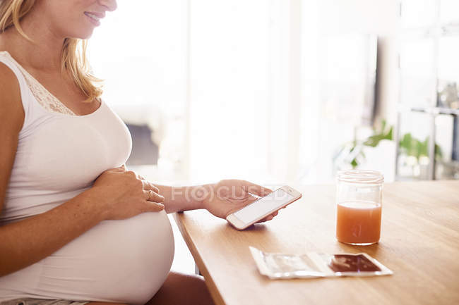 Pregnant woman looking at smartphone and ultrasound pictures — Stock Photo