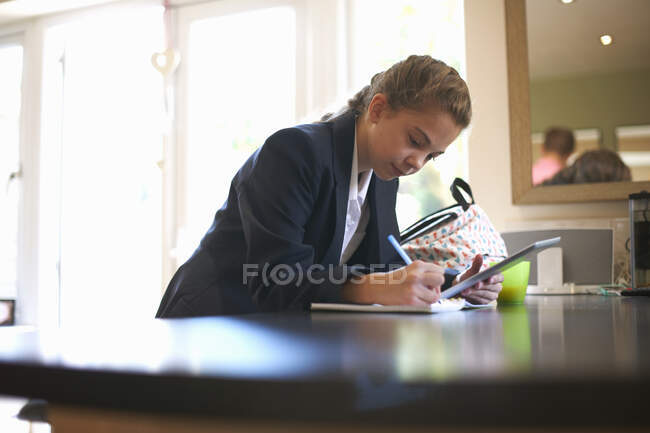 Adolescente colegiala haciendo la tarea en el mostrador de cocina - foto de stock