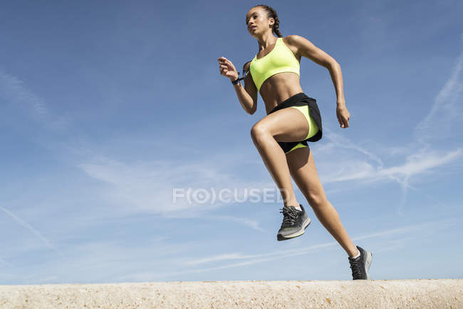 Низкий угол обзора молодой женщины, бегущей против голубого неба — стоковое фото