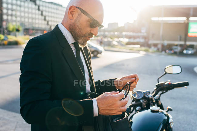 Mature businessman beside motorcycle holding eyeglasses — Stock Photo