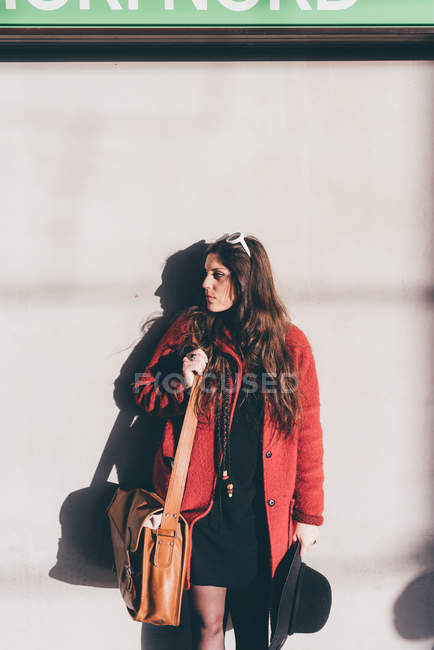Молодая женщина стоит на улице, тень бросается на стену позади нее — стоковое фото
