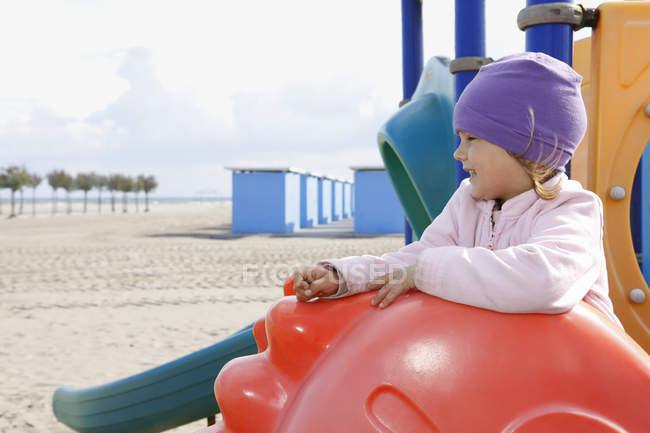 Menina no parque infantil equipamento na praia olhando para longe — Fotografia de Stock