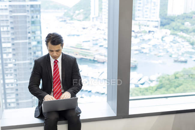 Uomo d'affari seduto sul davanzale della finestra e utilizzando il computer portatile — Foto stock