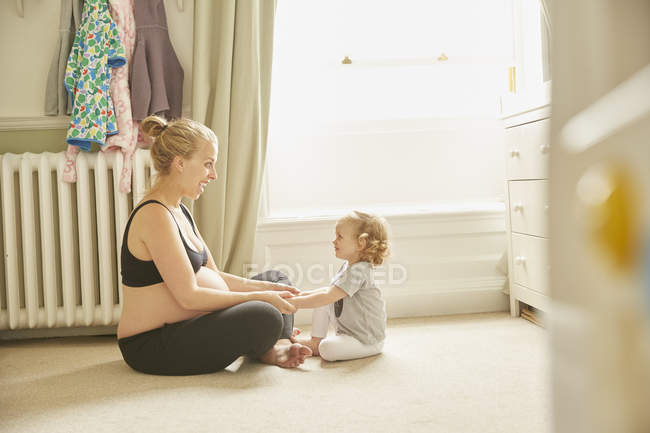 Вид сбоку на беременную женщину и дочь в спальне — стоковое фото