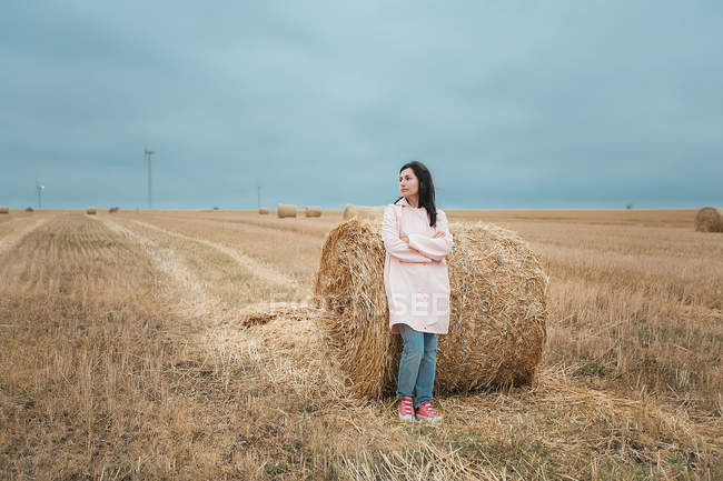 Женщина в розовом плаще, стоящая у стога сена — стоковое фото