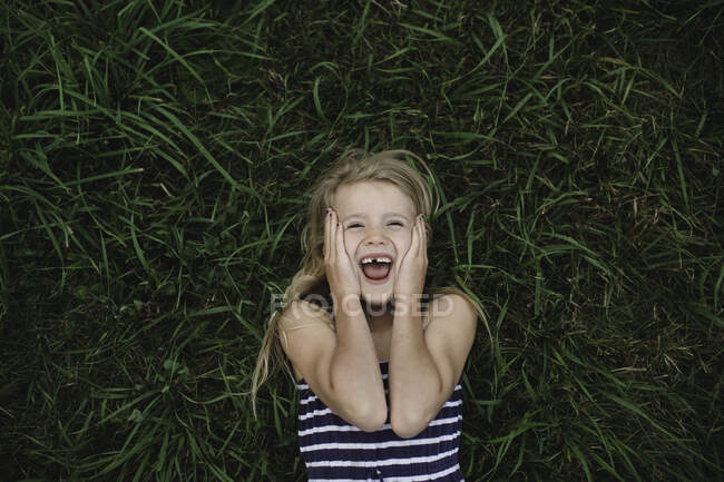 Retrato de chica acostada en la hierba con las manos en las mejillas - foto de stock