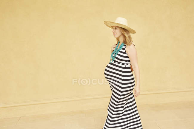 Mujer embarazada caminando por la pared amarilla - foto de stock
