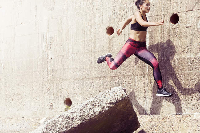 Young female free runner jumping across sea wall — Stock Photo