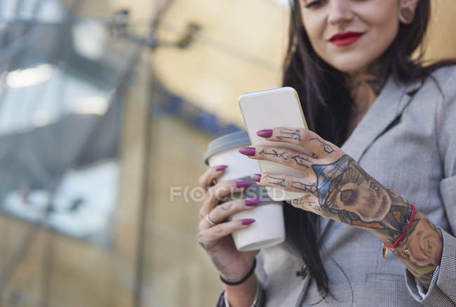 Businesswoman holding coffee cup and smartphone outdoors — Stock Photo