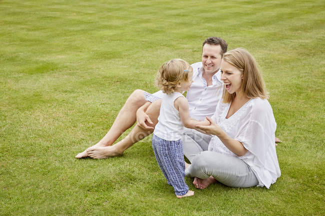 Couple with daughter sitting on green lawn — Stock Photo
