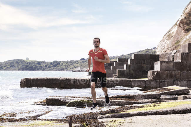 Jovem correndo ao longo da borda da água do mar — Fotografia de Stock