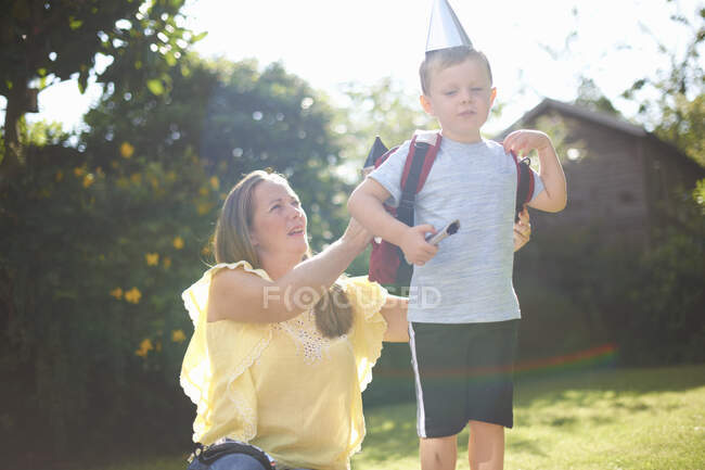 Reife Frau legt im Garten Rucksack mit Raketenkostüm auf Sohn — Stockfoto