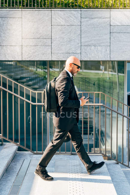Зрелый бизнесмен выходит на улицу, используя смартфон — стоковое фото