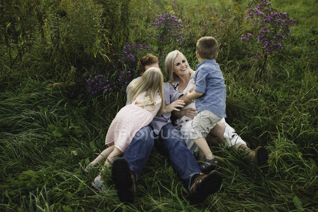 Pais e filhos deitados na grama alta juntos — Fotografia de Stock