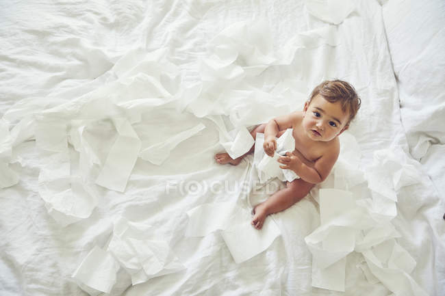 Niño sentado en la cama, sosteniendo un rollo de inodoro deshilachado - foto de stock
