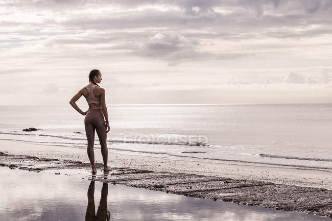 Молодая бегунья на пляже смотрит на море — стоковое фото