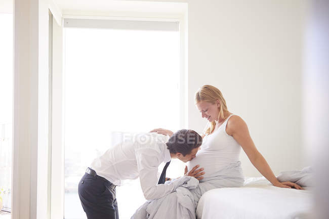 Man kissing pregnant girlfriend in stomach in bedroom — Stock Photo