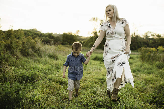 Madre e hijo caminando sobre hierba tomados de la mano - foto de stock