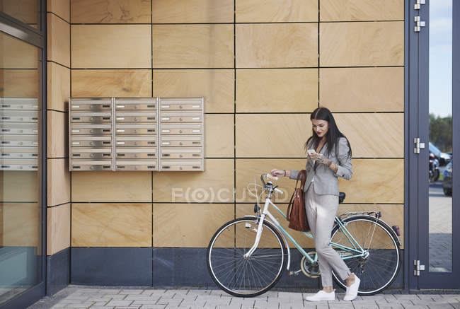 Businesswoman with bicycle and smartphone near office building — Stock Photo