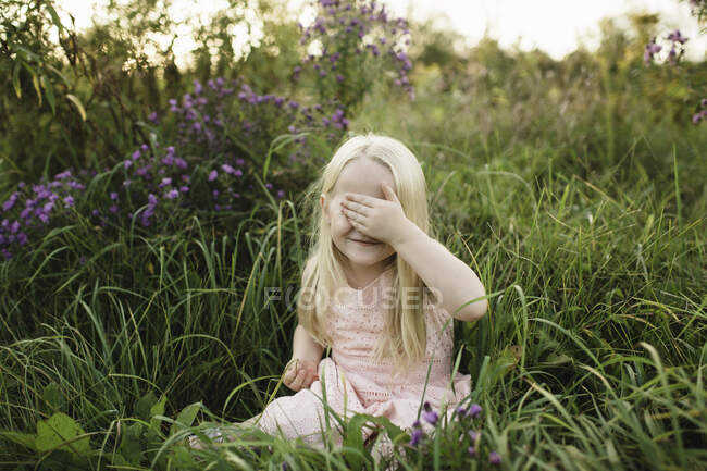 Chica sentada en la hierba alta, la mano cubriendo los ojos - foto de stock
