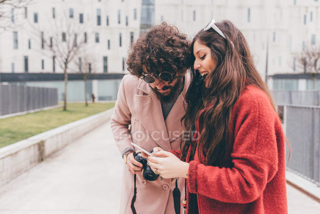 Coppia giovane in piedi all'aperto, guardando smartphone, ridendo — Foto stock