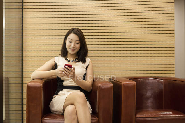 Geschäftsfrau sitzt mit Smartphone im Ledersessel — Stockfoto