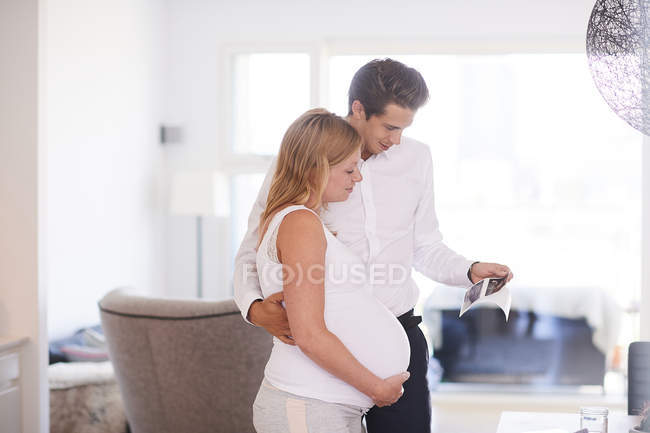 Schwangere betrachten Ultraschallbilder im Wohnzimmer — Stockfoto
