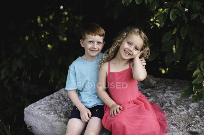 Retrato de niño y hermana sentados en la roca - foto de stock