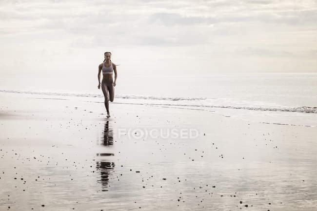 Mujer joven corriendo a lo largo de la playa - foto de stock