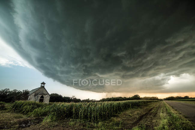 Supercell se avecina en la distancia, iglesia abandonada en primer plano, Miltonvale, Kansas, EE.UU. - foto de stock