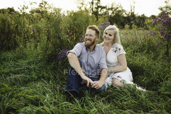 Paar sitzt im hohen Gras und schaut lächelnd weg — Stockfoto