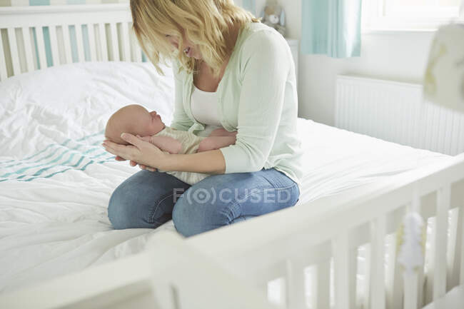 Mère assise sur le lit, tenant le nouveau-né — Photo de stock