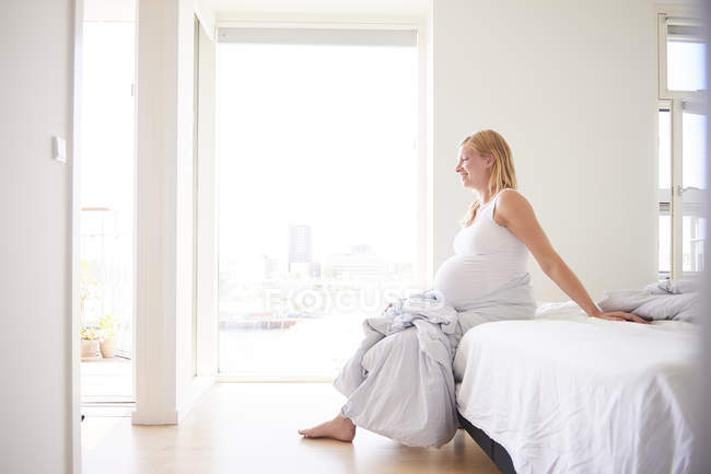 Schwangere junge Frau sitzt auf Bett — Stockfoto